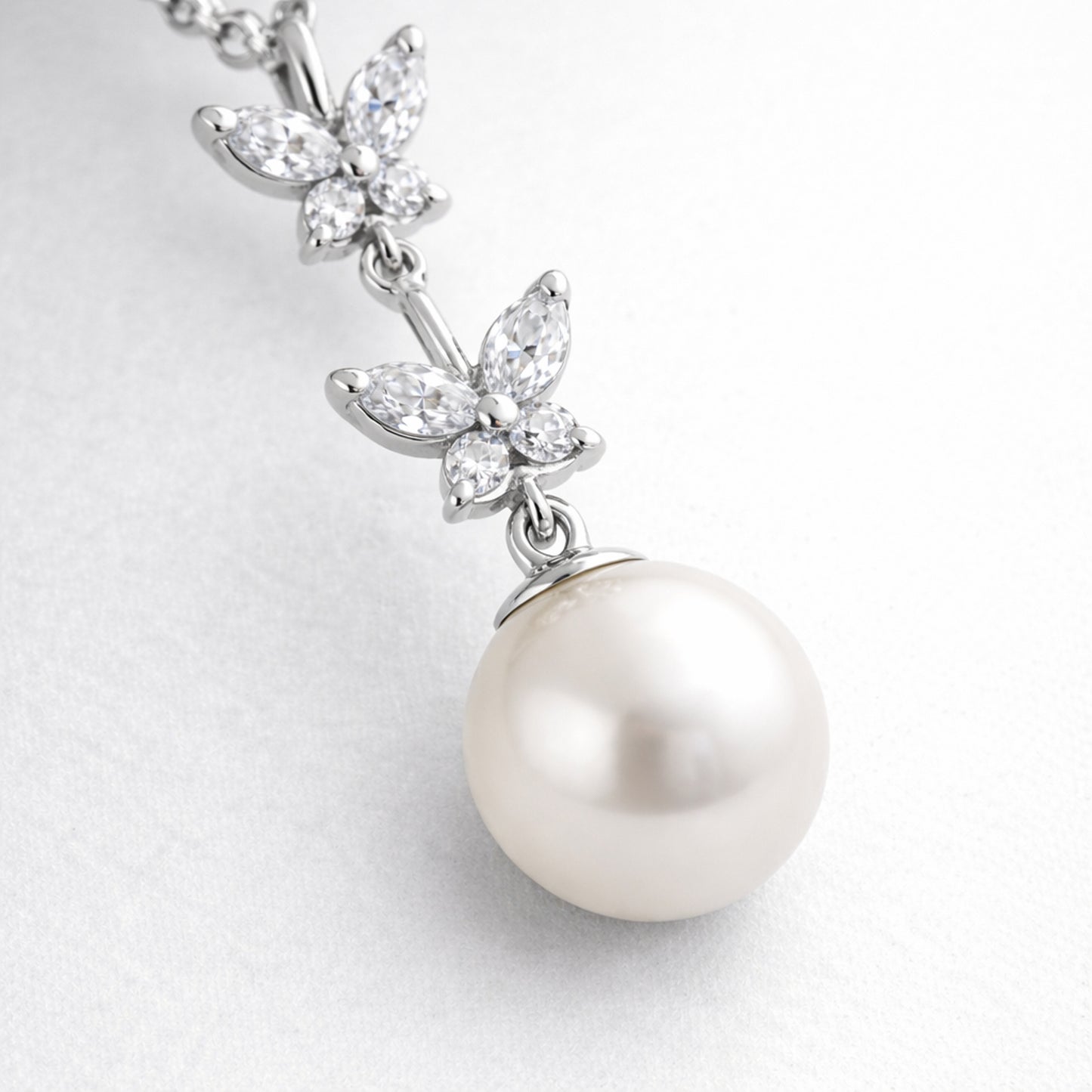 Close up view of the butterfly drop pendant focusing on the prong set cubic zirconia elements and smooth pearl surface.