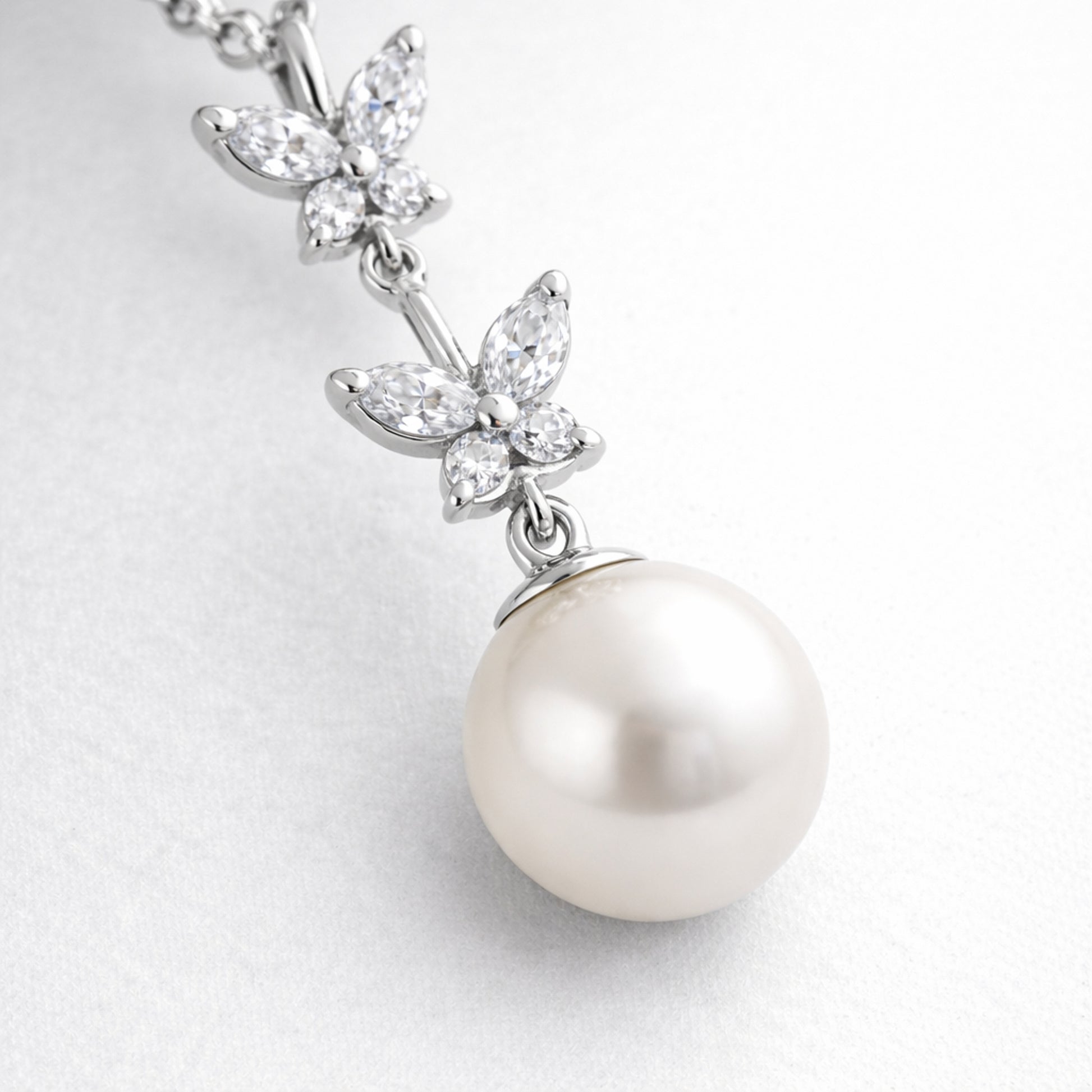 Close up view of the butterfly drop pendant focusing on the prong set cubic zirconia elements and smooth pearl surface.