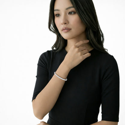 Editorial model shot pairs a black short-sleeve dress with a slim silver tone cuff lined in continuous clear crystals, showing its refined sparkle on the wrist.