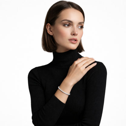 Studio shot shows a slim silver tone cuff edged with clear channel-set crystals on a model in a black ribbed turtleneck, highlighting sleek wrist sparkle.