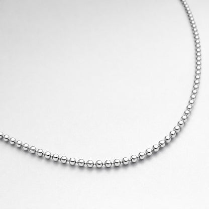 Close up studio image showing the polished round beads of a silver tone beaded chain necklace.