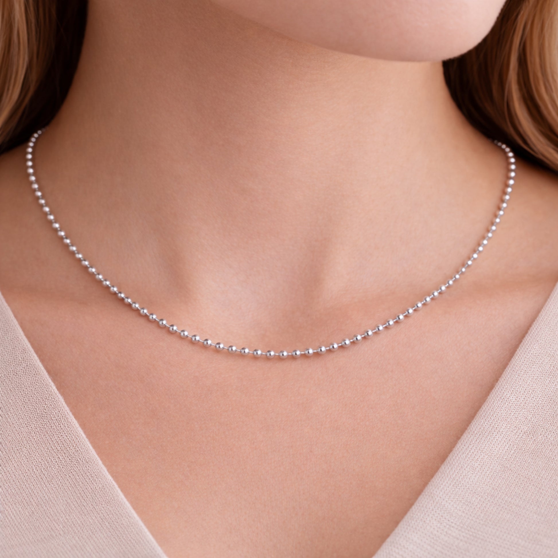 Lifestyle image of a silver tone beaded chain necklace worn on the neck showing its delicate drape.