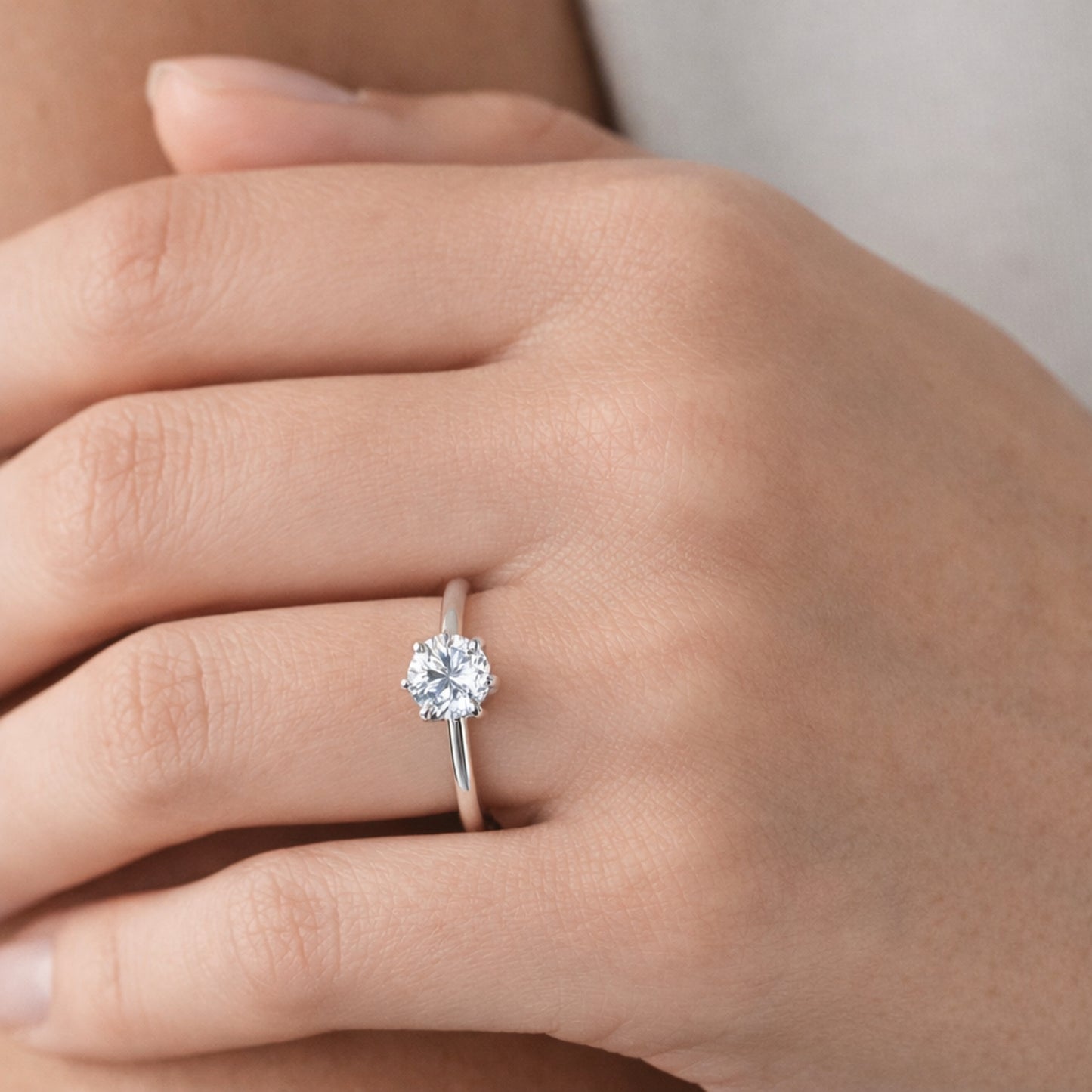 Close up worn on hand view of the classic solitaire cubic zirconia ring highlighting the slim silver tone band and the single round cut stone in a raised prong setting.