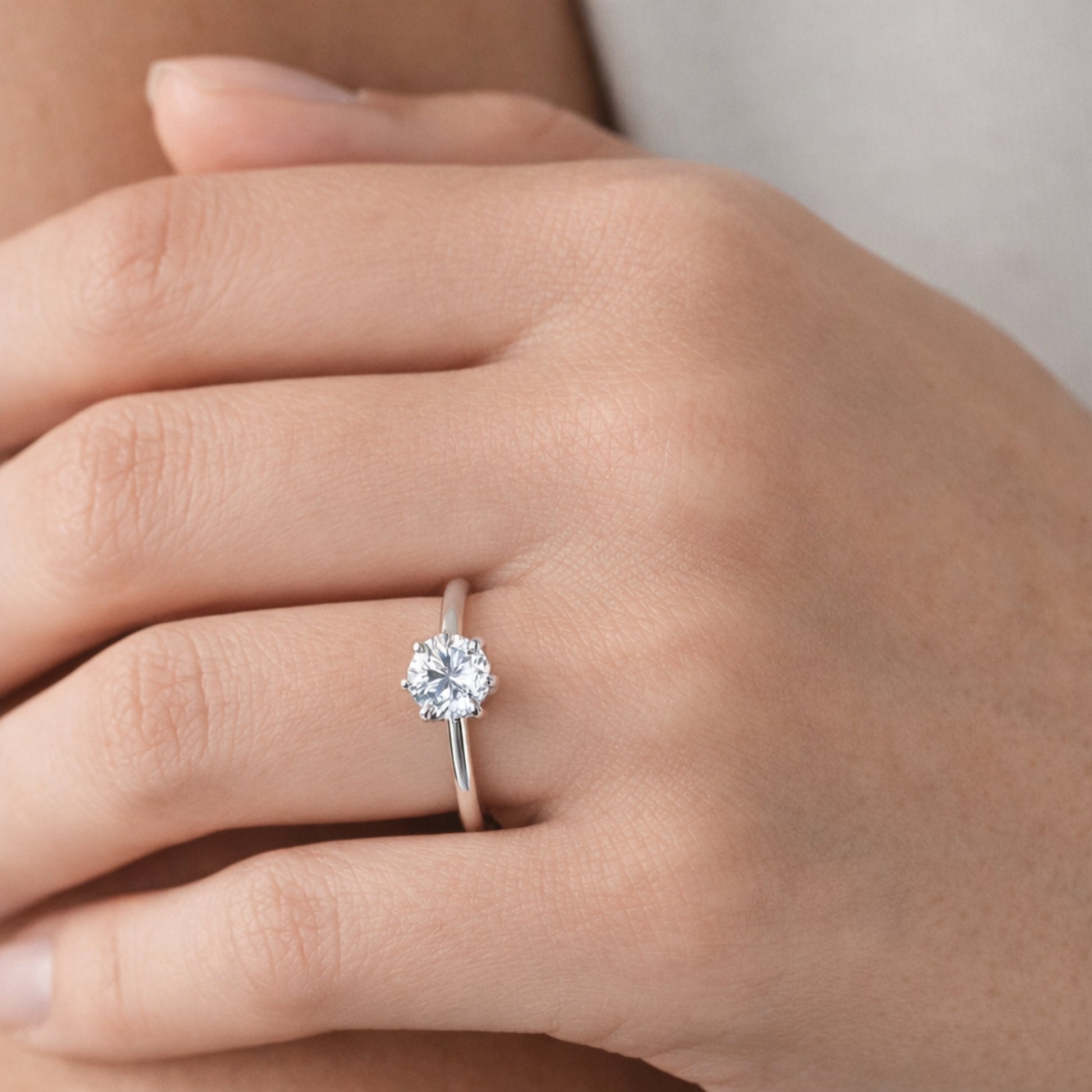 Close up worn on hand view of the classic solitaire cubic zirconia ring highlighting the slim silver tone band and the single round cut stone in a raised prong setting.