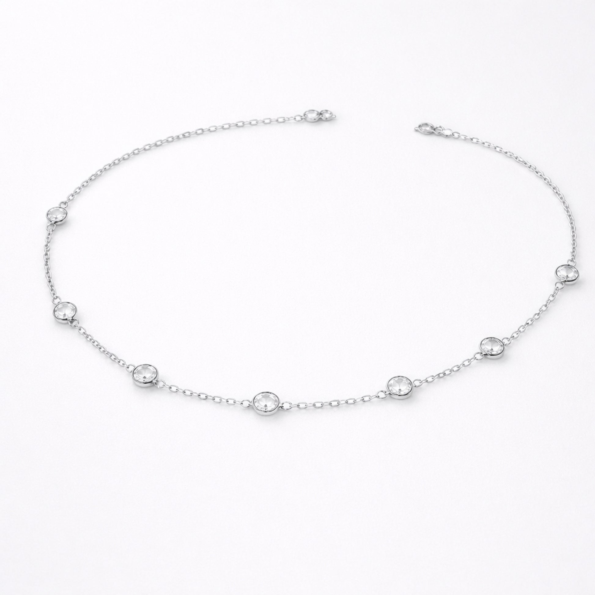 Styled lifestyle image of a station necklace worn close to the collarbone, showcasing the elegant placement of bezel set stones in silver tone.