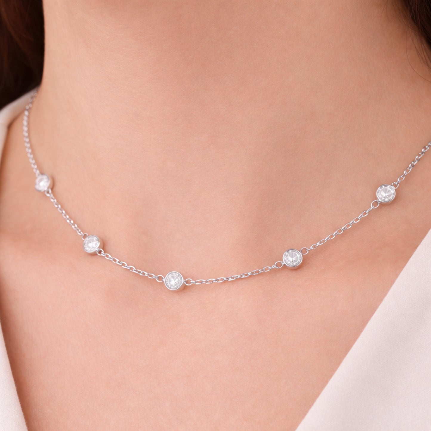 Detail view of the silver tone station necklace worn on the neck, highlighting the bezel set stone spacing and polished metal finish.