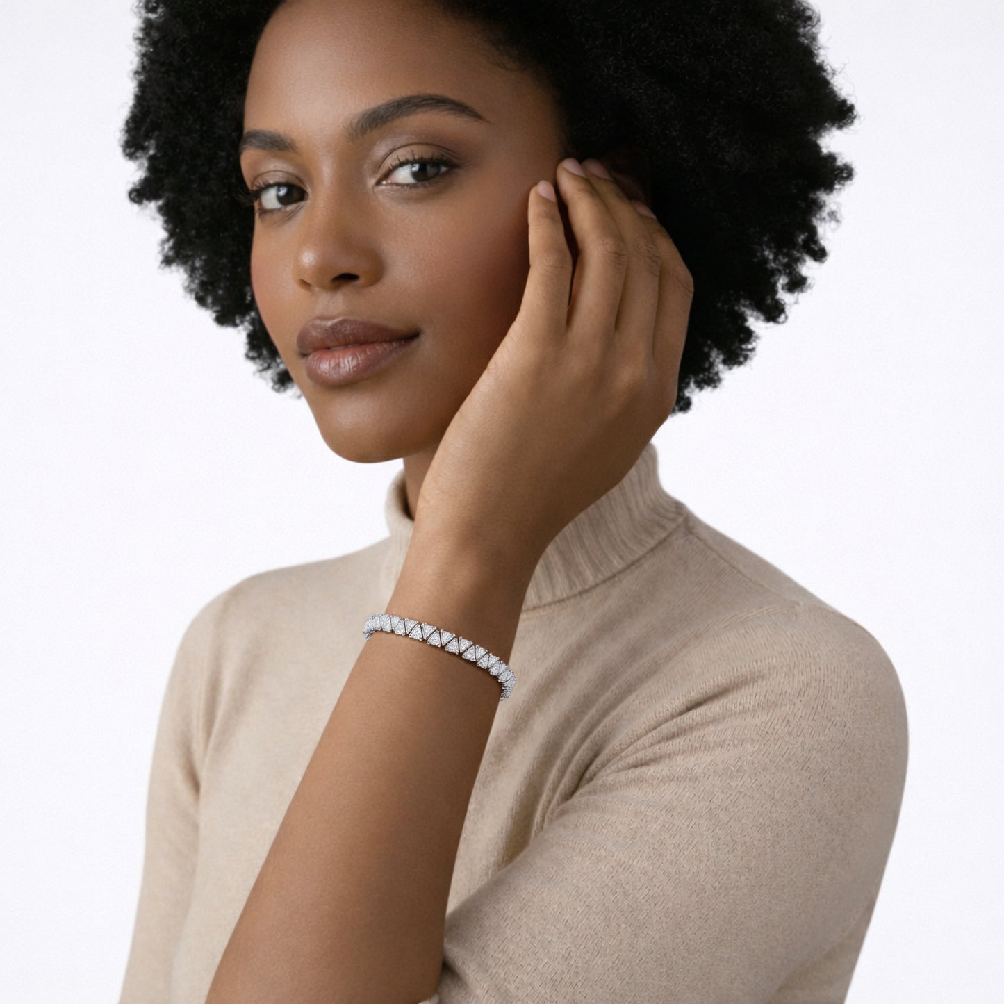 On-model portrait shows a geometric silver tone tennis bracelet lined with large cubic zirconia stones wrapping a wrist above a beige turtleneck, delivering crisp sparkle.
