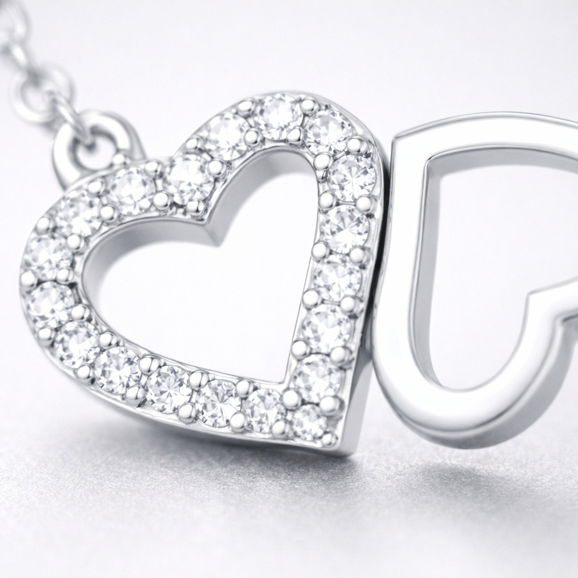 Close up view of the double heart pendant highlighting the pavé set heart and the polished open heart design.