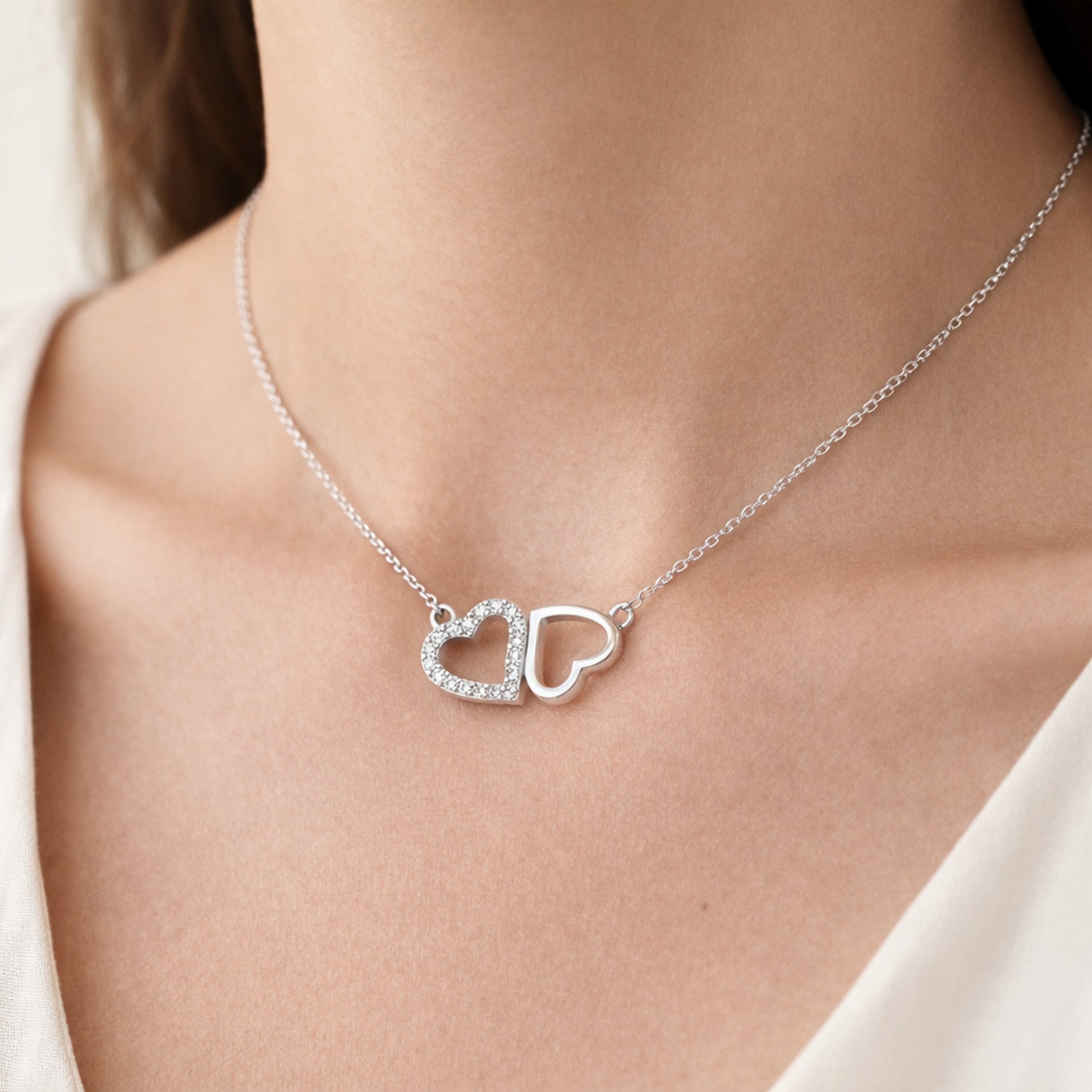 Worn view of a double heart pendant featuring one cubic zirconia accented heart and one open heart design.