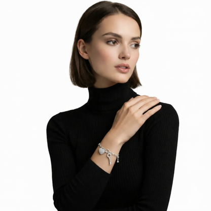 Model view features a silver tone charm bracelet with a pavé heart padlock, petite key, and polished links draped over a black ribbed sleeve for crisp contrast.