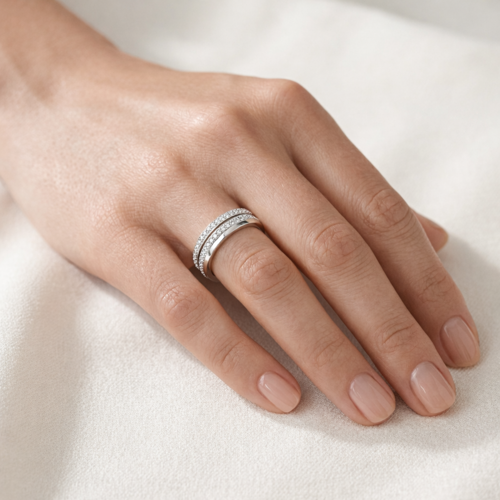 Worn view of the intertwined silver tone ring showing two pavé set cubic zirconia bands and one smooth polished band to illustrate fit and proportions.