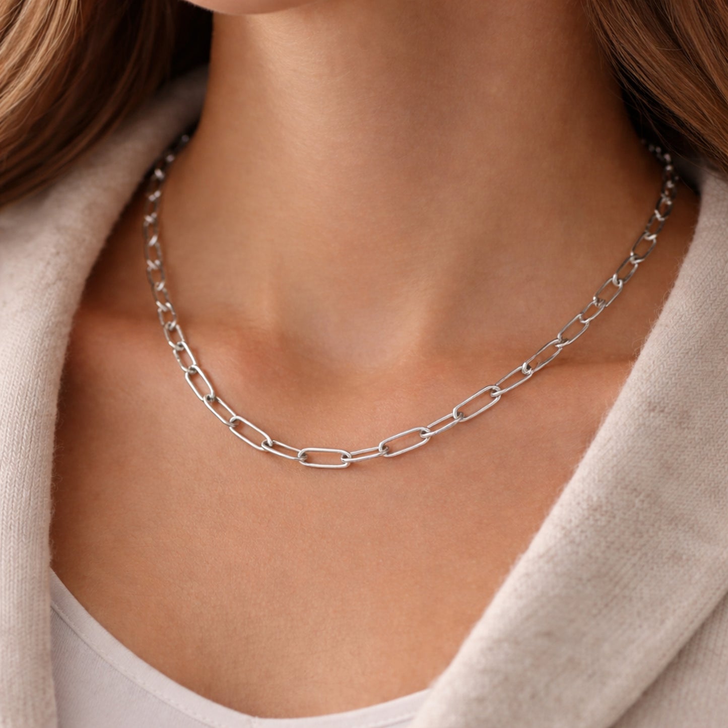 Lifestyle image of a silver tone paperclip chain necklace worn on the neck highlighting its contemporary style.