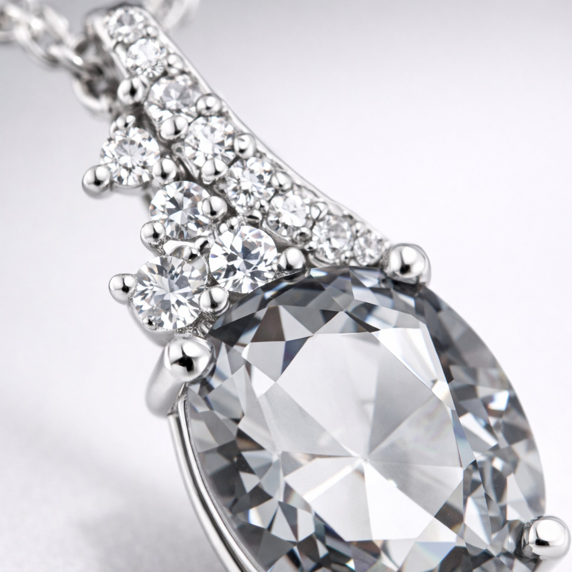 Close up view of the pear cut cubic zirconia pendant focusing on the faceted stone and silver tone prong setting with accent stones.