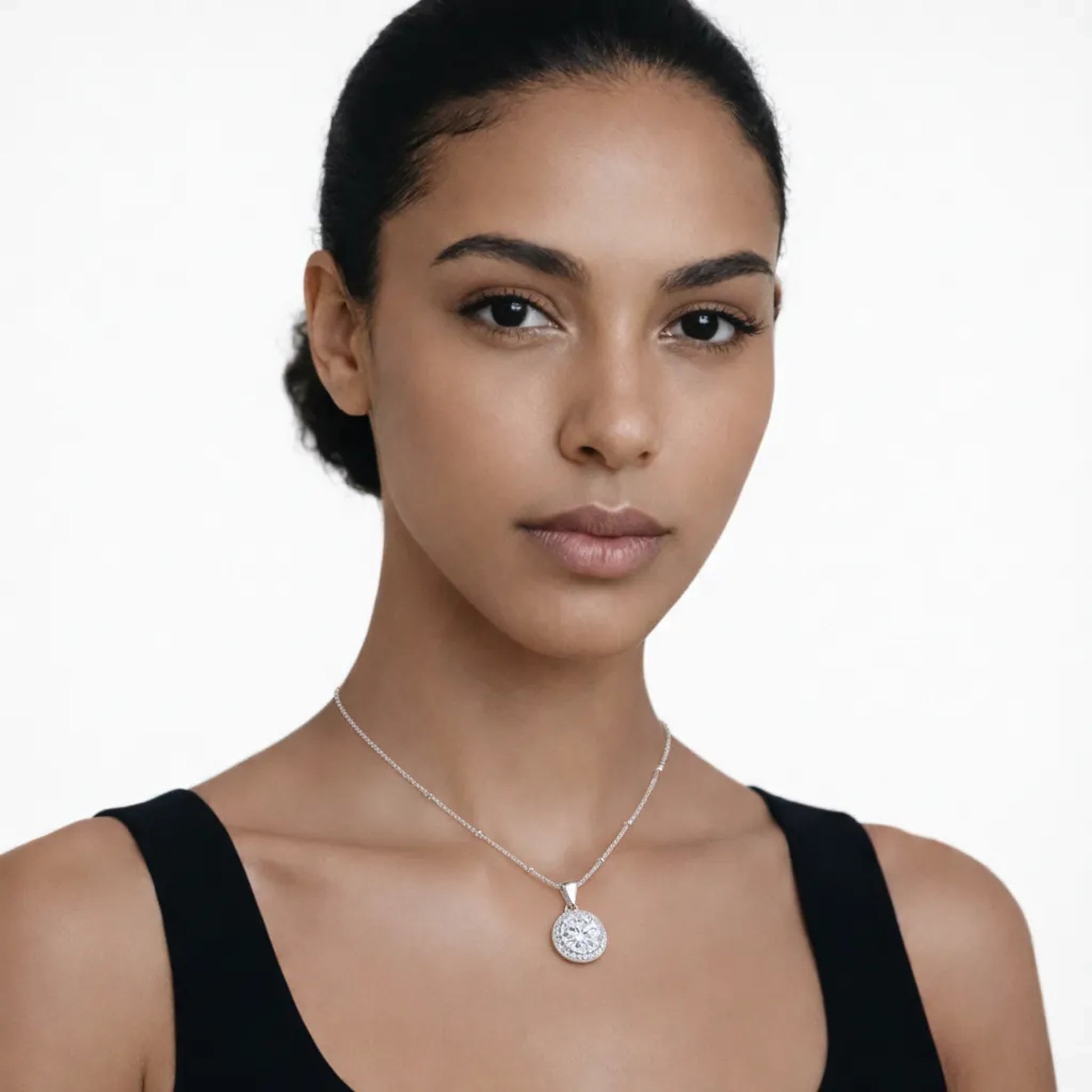 On-model portrait highlights a silver tone round halo cubic zirconia pendant, styled with a black scoop-neck top so the pendant stays centered at the neckline.