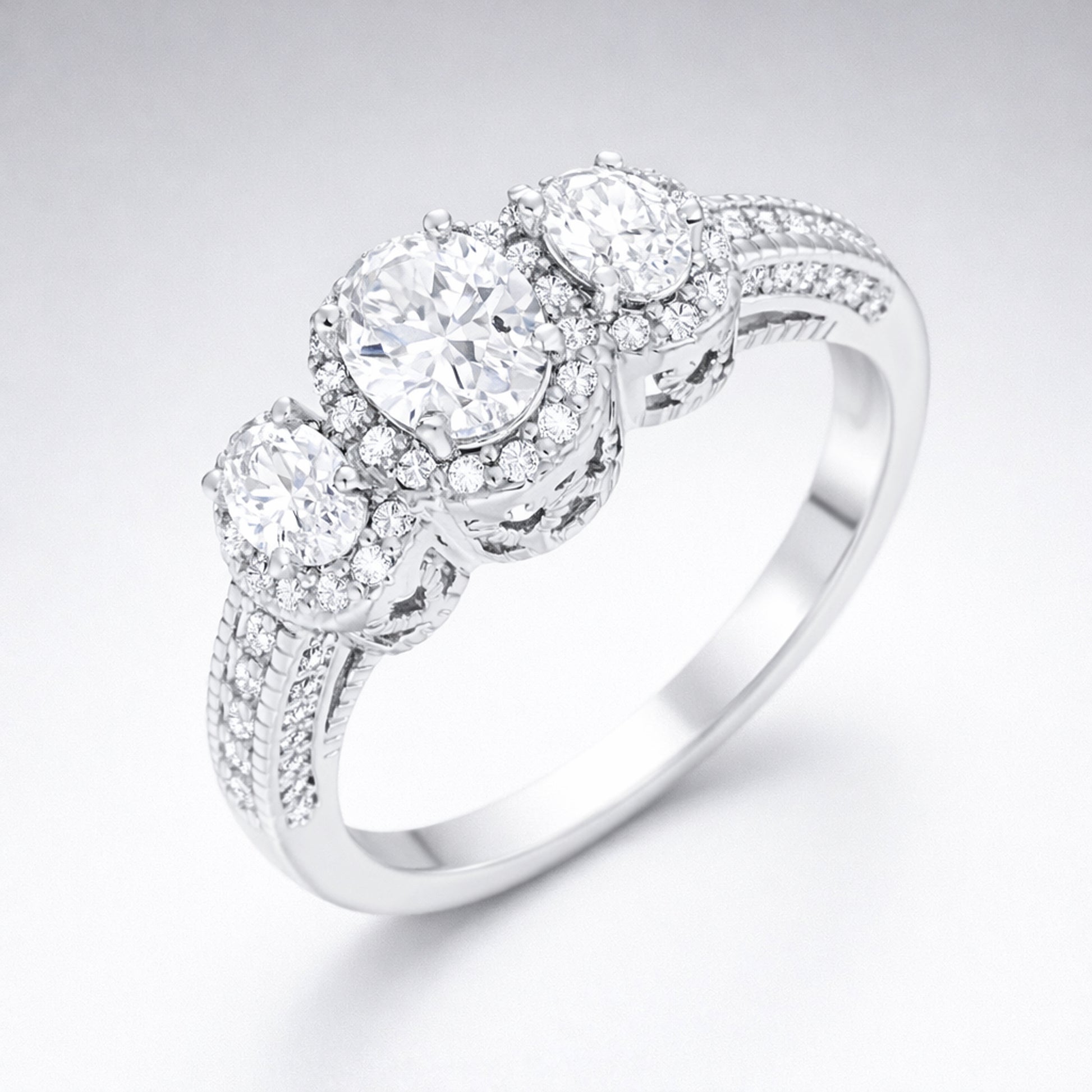 Angled studio view of a three stone halo cubic zirconia ring in silver tone finish, showing the raised settings and pavé accented band.