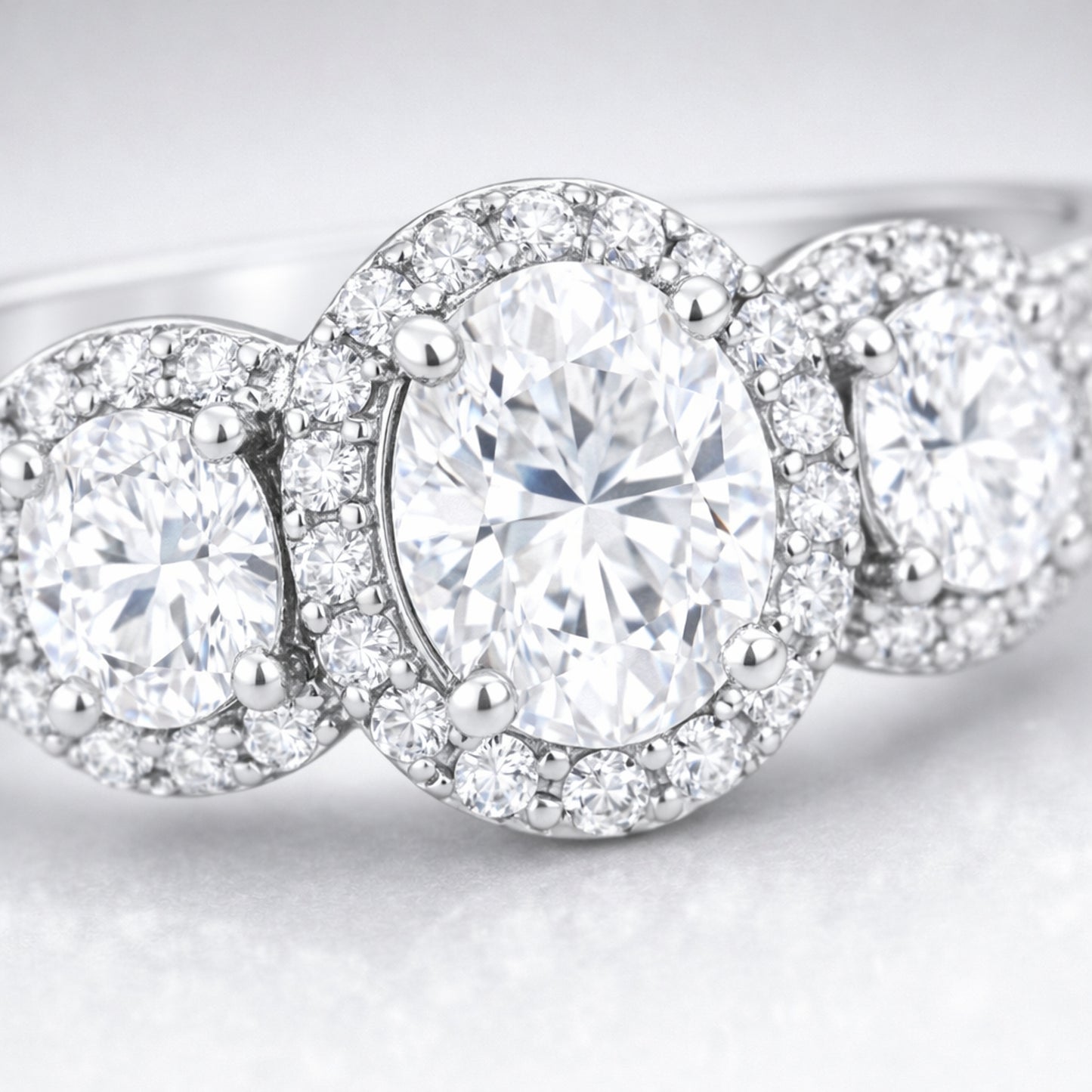 Close up view of a three stone halo cubic zirconia ring in silver tone finish, highlighting the central round stone flanked by two smaller round stones with pavé halos.