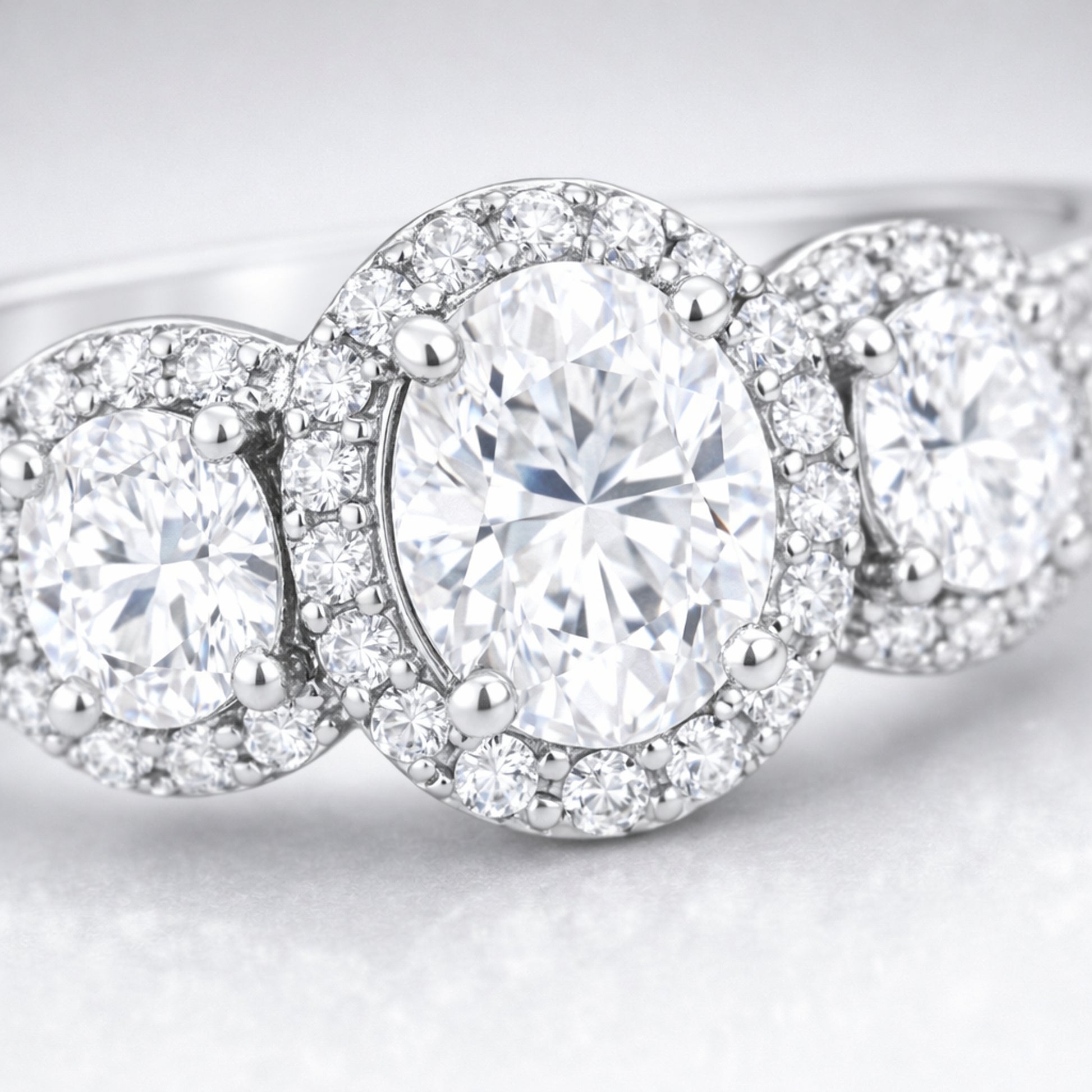 Close up view of a three stone halo cubic zirconia ring in silver tone finish, highlighting the central round stone flanked by two smaller round stones with pavé halos.