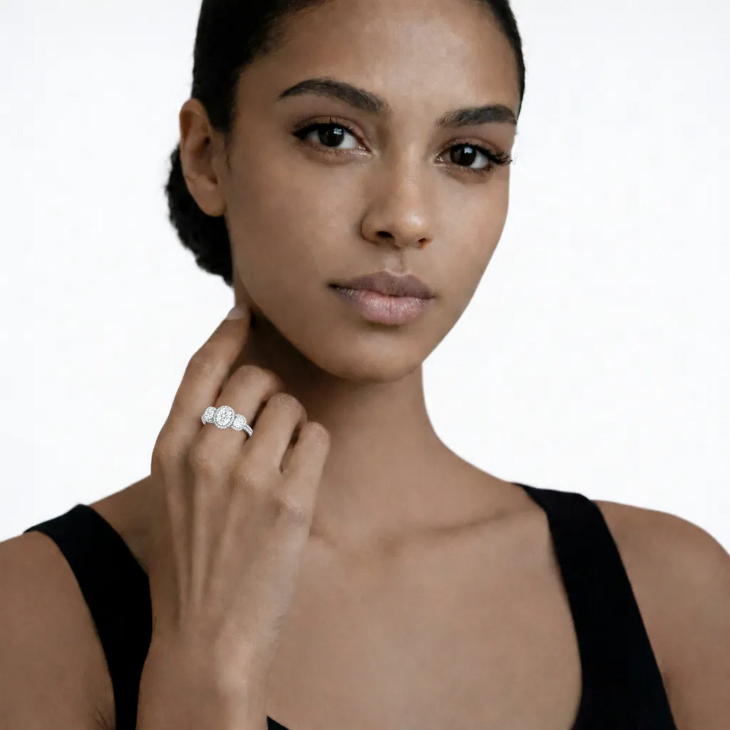 On-model portrait highlights a silver tone three stone halo cubic zirconia ring, styled with a black sleeveless top so the ring sparkles along the fingertips.